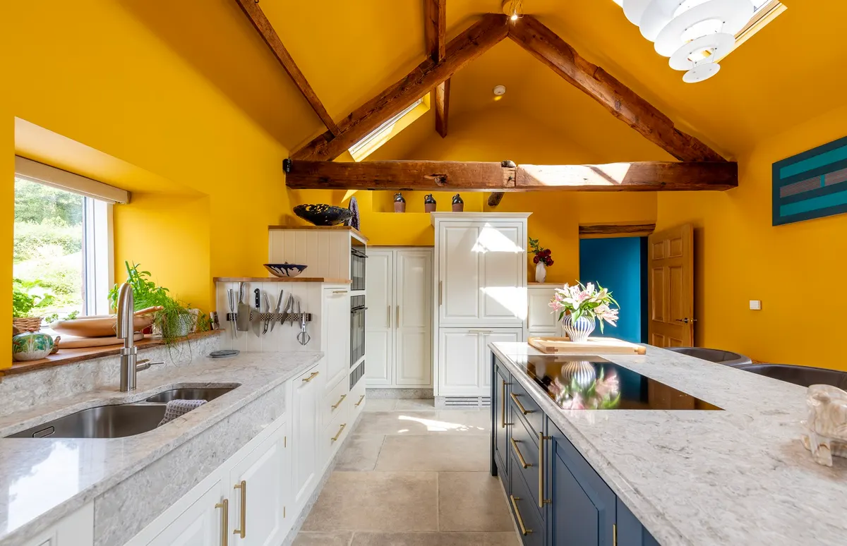 Barn conversion kitchen near Bassenthwaite under an exposed king-post truss, with a navy island and pale in-frame cabinets