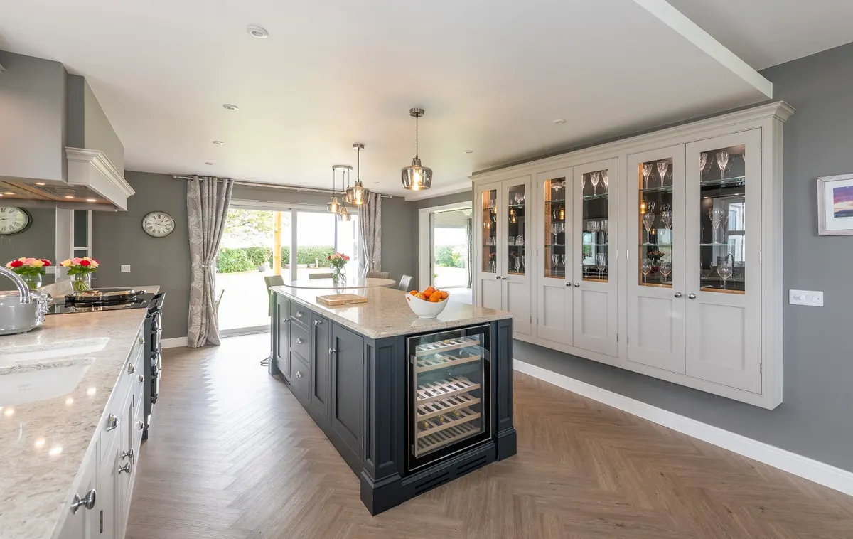 Open-plan hand-painted kitchen at Burgh by Sands with a navy island, integrated wine store and a glazed dresser run over herringbone parquet