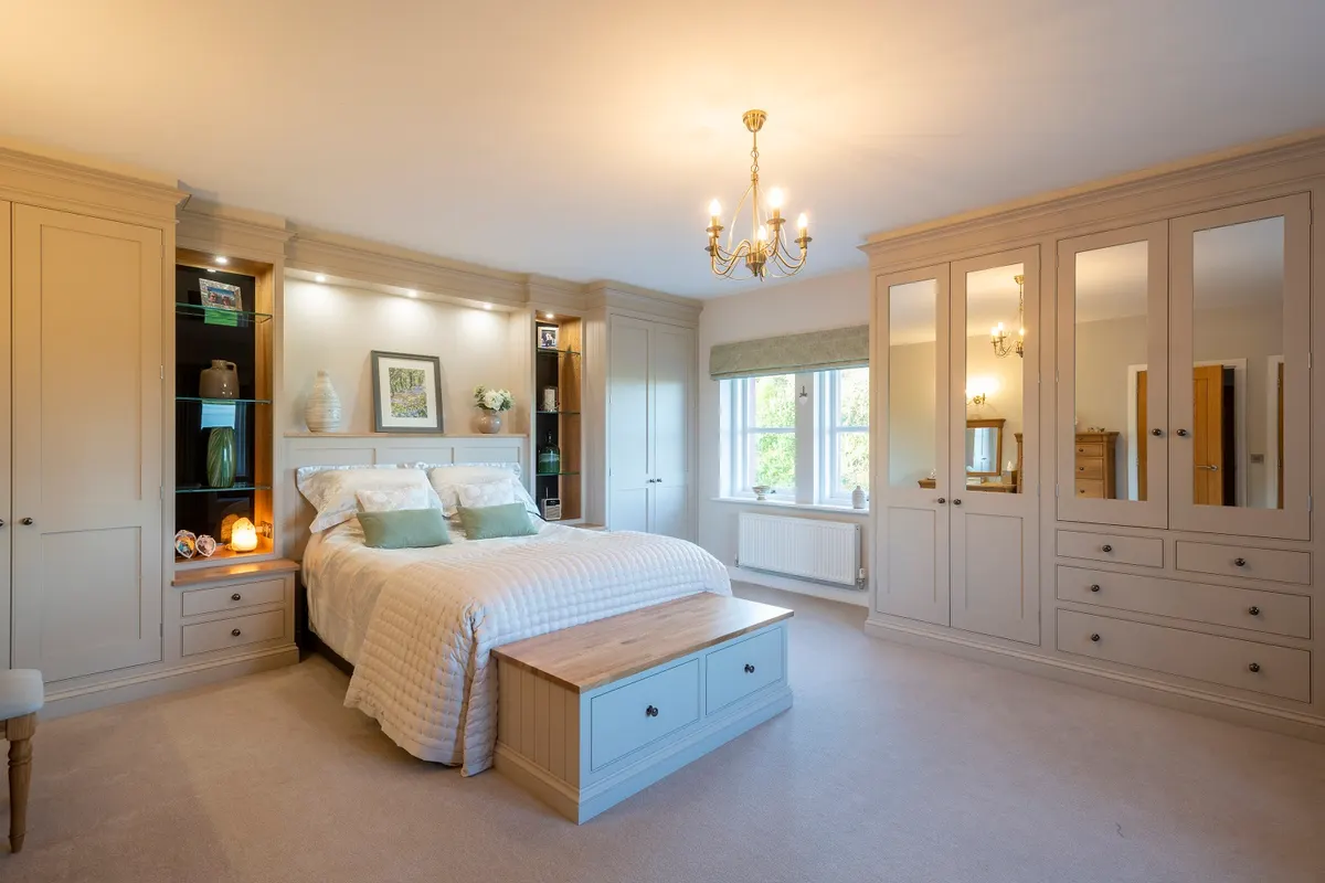 Fitted bedroom in cream, with mirrored wardrobe doors, a dressing area and lit display cabinets