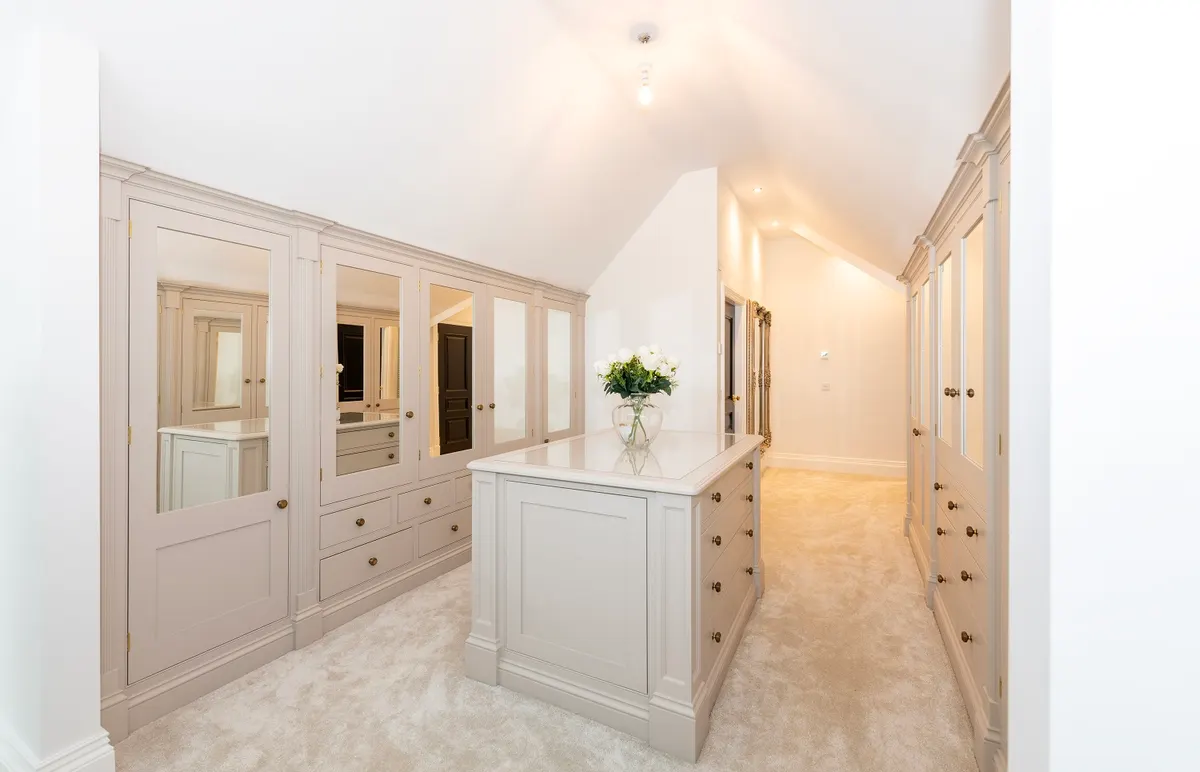 Fitted dressing room at Dornock with mirrored wardrobe fronts down both walls and a free-standing island of drawers