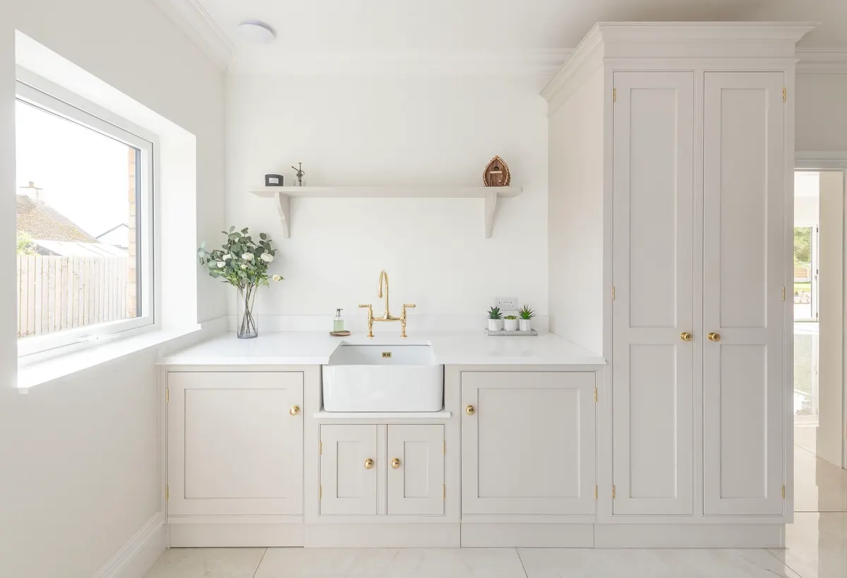Utility room at Dornock with a butler sink, brass tap and open shelves set into pale in-frame cabinets
