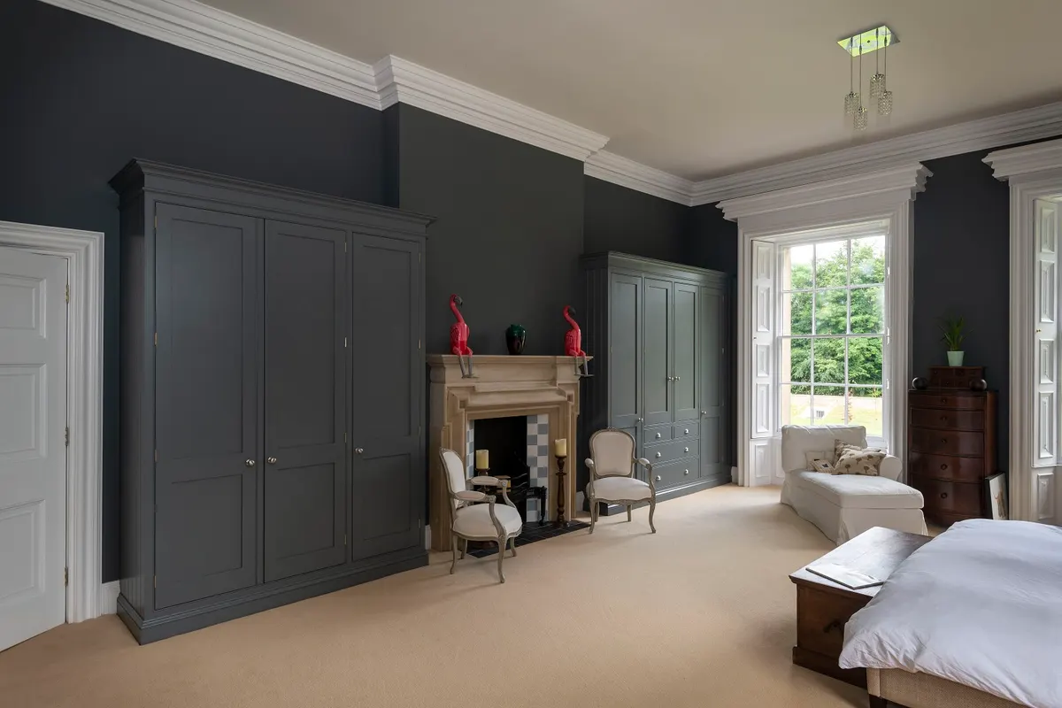 Fitted bedroom in grey, with full-height wardrobes either side of a stone fireplace