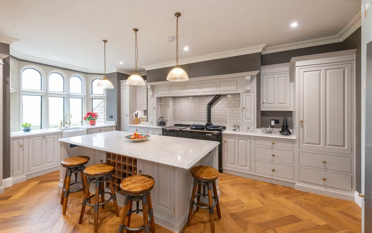 Kitchen at Carrfoot Lodge, Mansergh, with arched windows, a white island and turned wooden stools