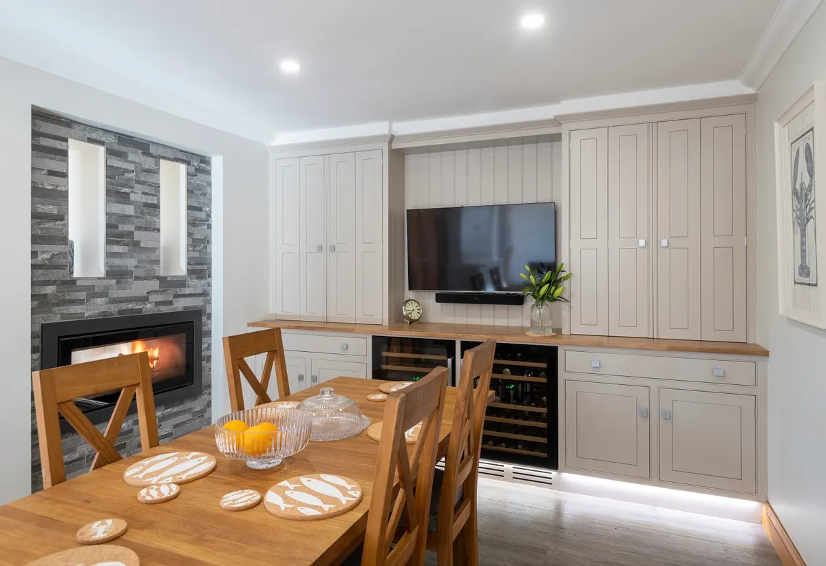 Fitted media wall beside a stone fireplace, with a television, a wine store and cabinets to the ceiling