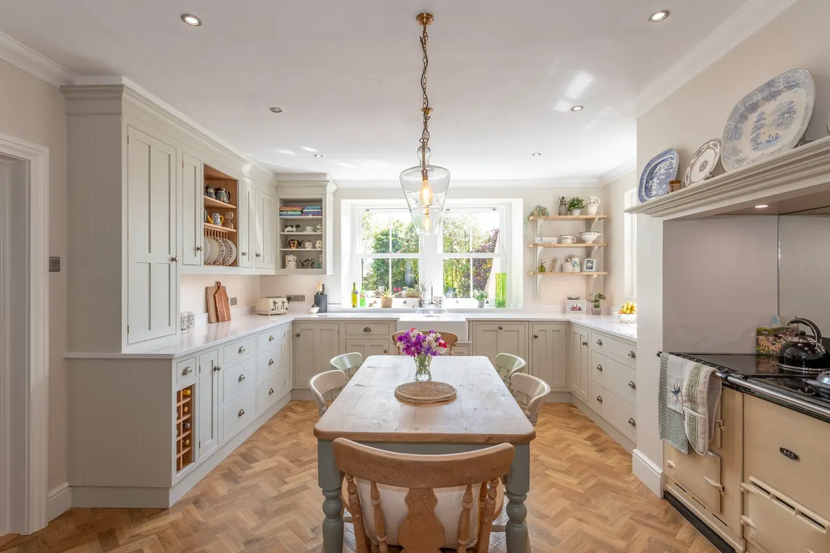 Cream in-frame kitchen at Red Hall with a plate rack, a range cooker and a pine table under the window