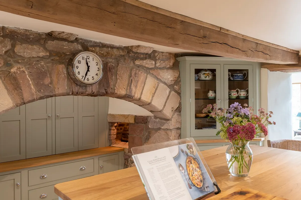 Cabinets fitted into a sandstone arch under a beam, with an oak worktop and a glazed dresser alongside