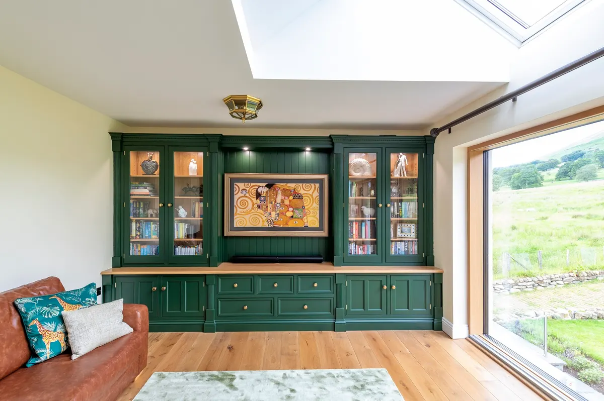 Fitted library and media wall at Threlkeld in deep green, glazed cabinets either side of the television, facing a window onto the fells