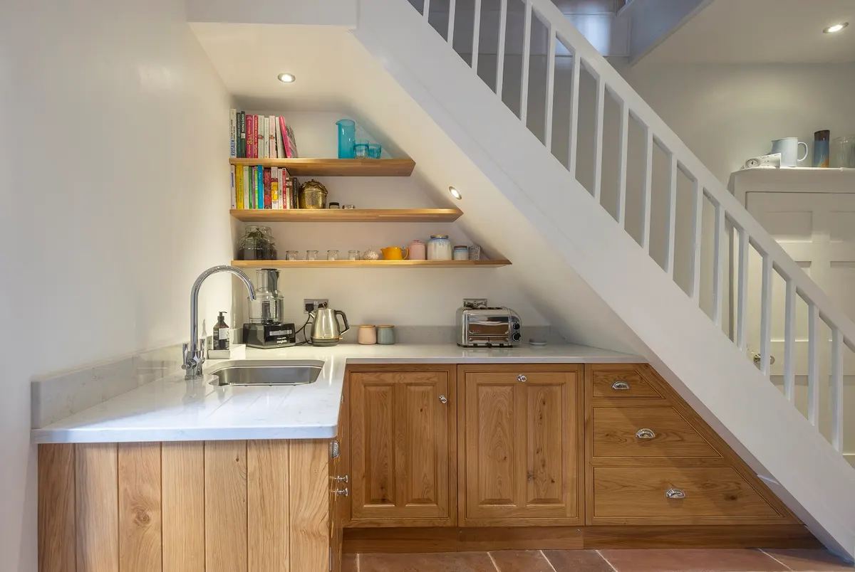 Small oak kitchen fitted under a staircase, worktop and shelves cut to follow the line of the stairs
