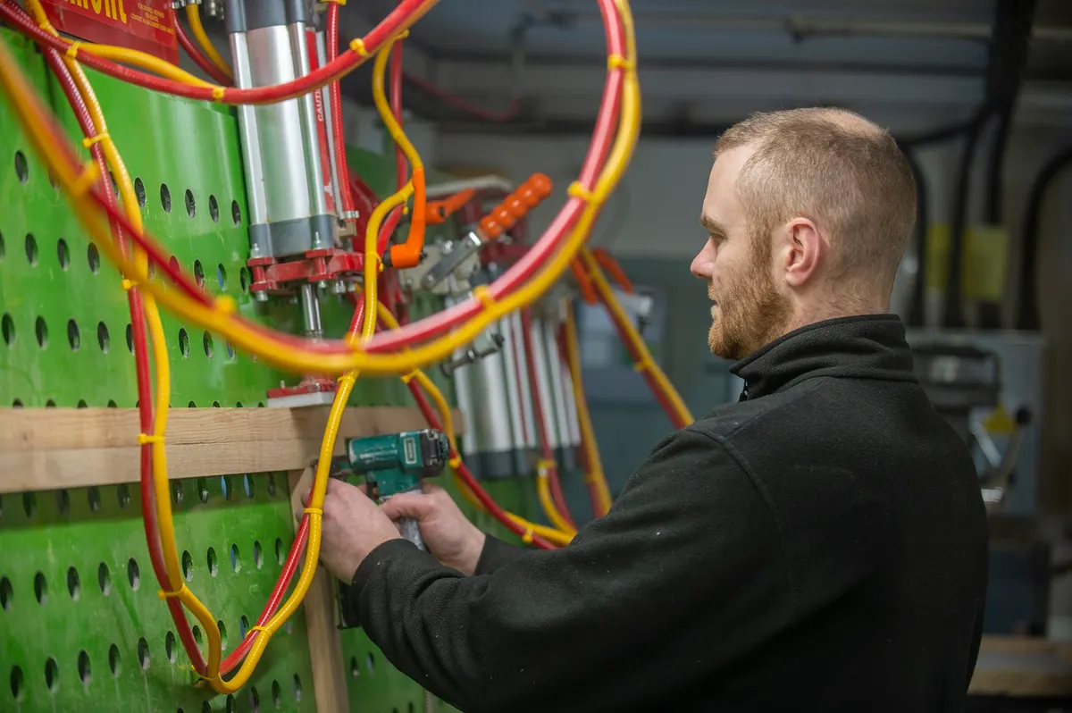 A joiner working an oak rail on the boring machine in the Thwaite Holme workshop at Dalston